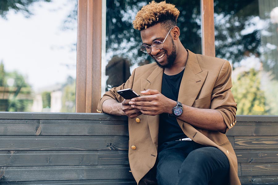 Contact Us - Stylish Young Man With Beard and Glasses on a Wooden Bench Using His Cell Phone
