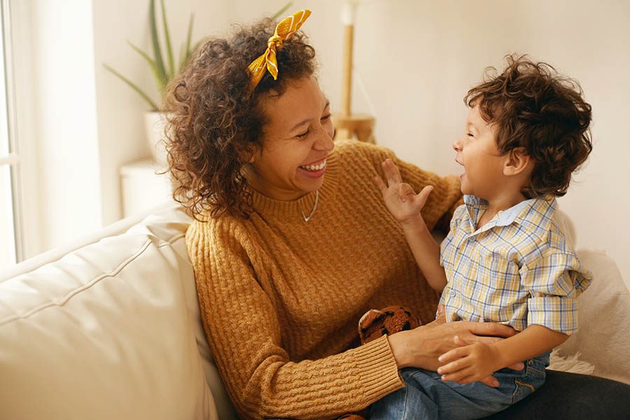 Personal Insurance - Mother and Toddler Son With Brown Curly Hair Laughing on a Leather Sofa in Their Living Room With Plants Behind Them
